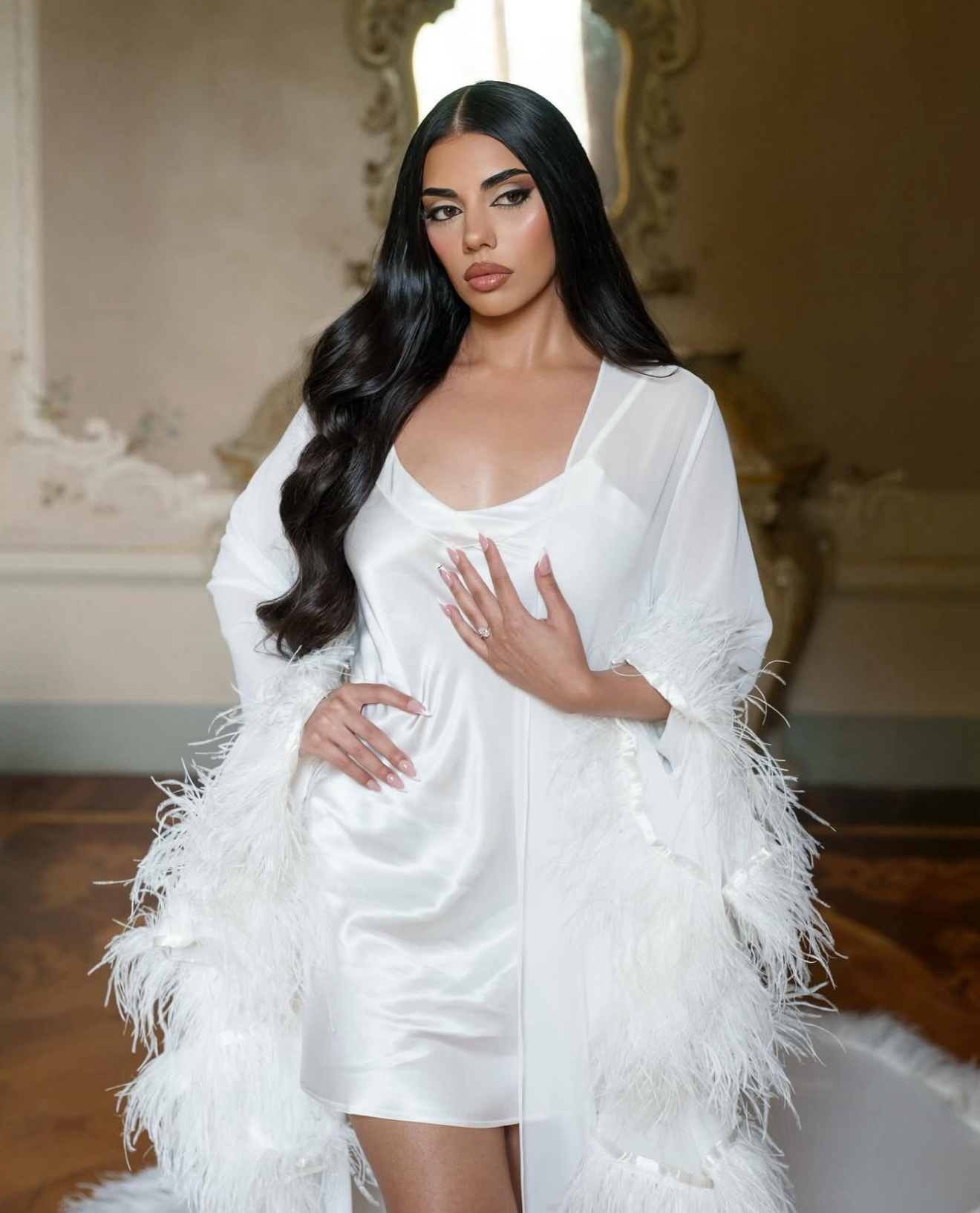 bride wearing a bridal robe with ostrich feathered sleeves in an elegant interior setting