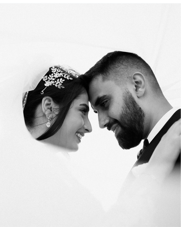 A bride and groom smiling at each other, with the bride wearing elegant Posy earrings