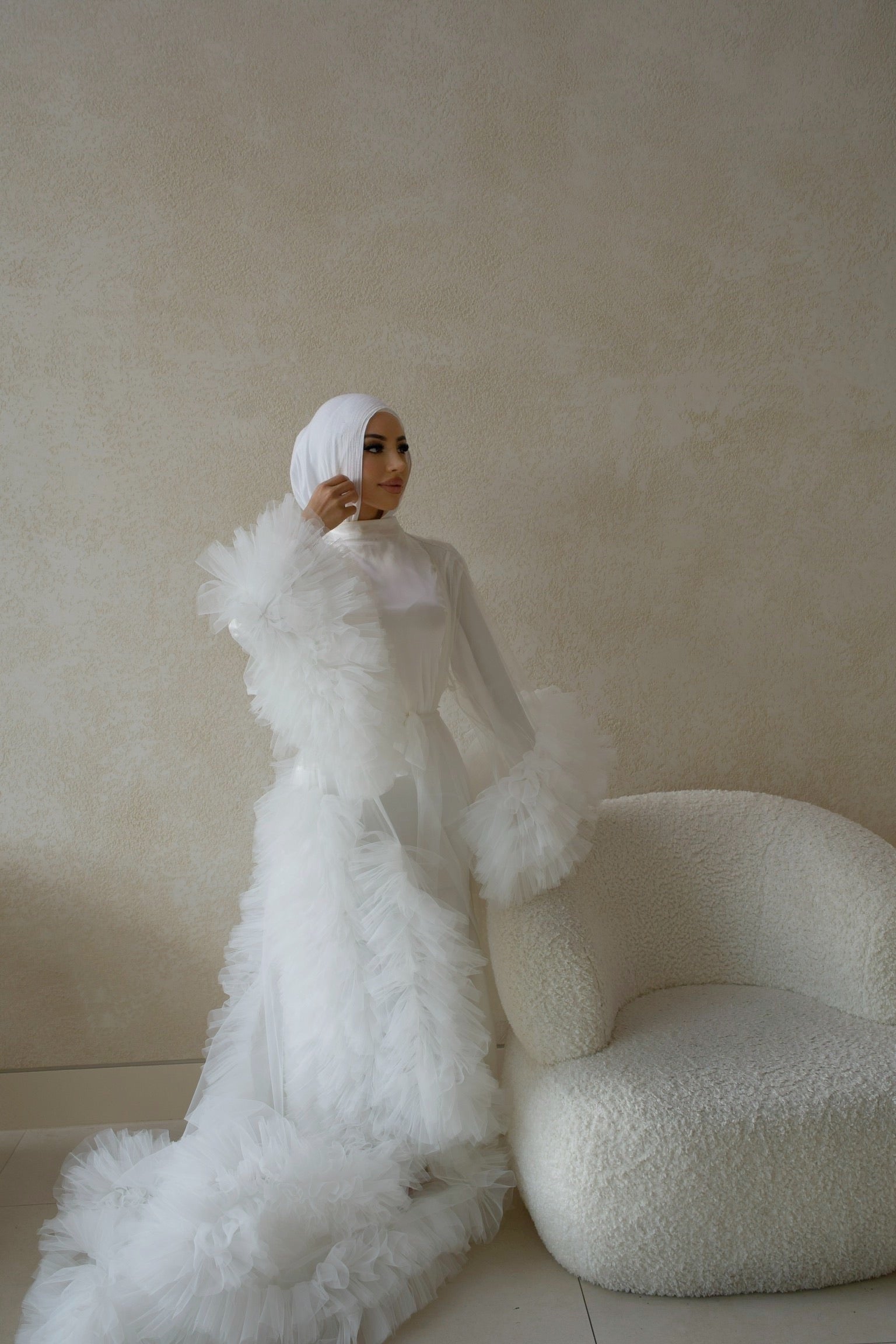 A woman in a white Elenora bridal ruffles robe beside a white chair