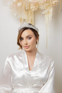Woman in bridal robe with crystal tiara, smiling for a photo