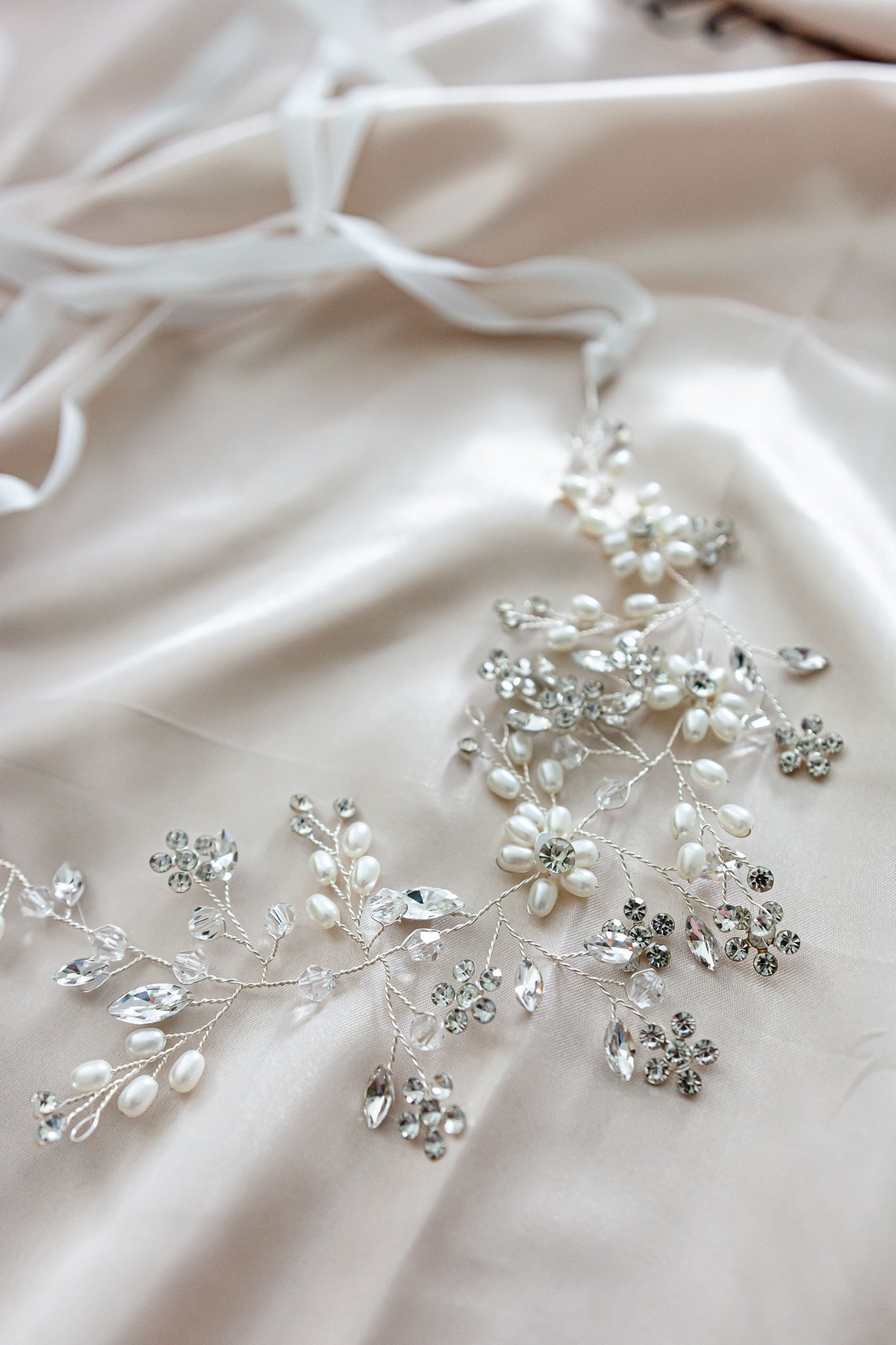 A close up of Aria white wedding floral headpiece with pearls and crystals in satin cloth