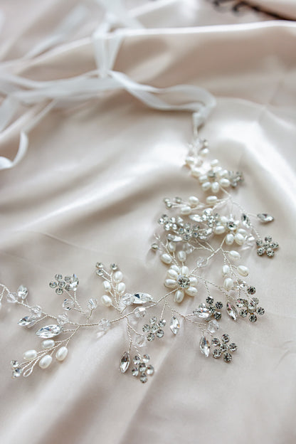 A close up of Aria white wedding floral headpiece with pearls and crystals in satin cloth