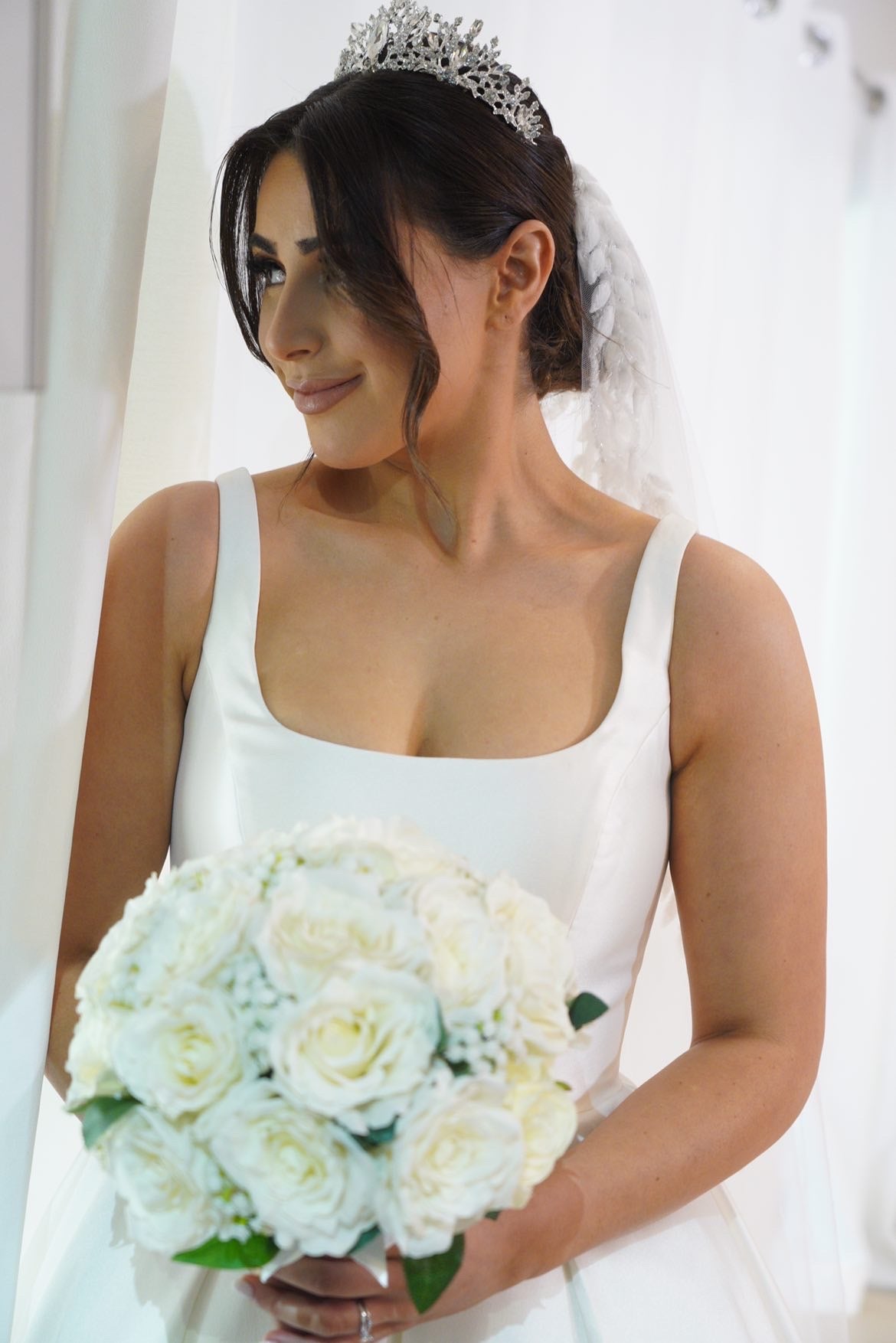 A bride in a white wedding gown holding a bouquet, wearing Estelle bridal tiara